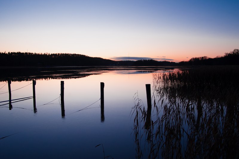 Kaarinan Voivalassa meren rannassa auringon viimeiset säteet värjäävät horisontin punertavaksi heijastuen peilityynestä vedestä, kun sinertävä pimeys alkaa jo laskeutua.