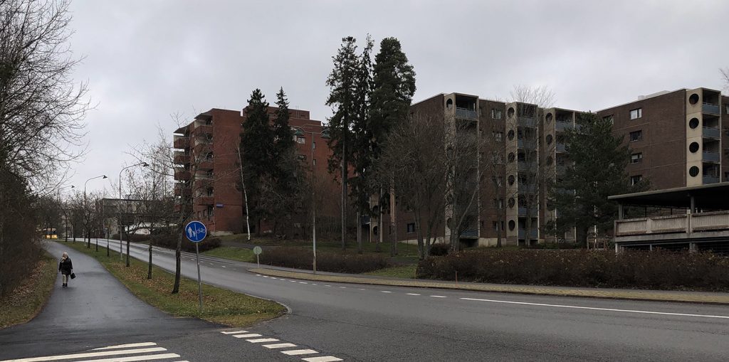 Turun Varissuon lähiön kerrostaloja marraskuun sateessa. Etualalla tie, jossa kulkee auto ja tien reunassa pyöräilijä.