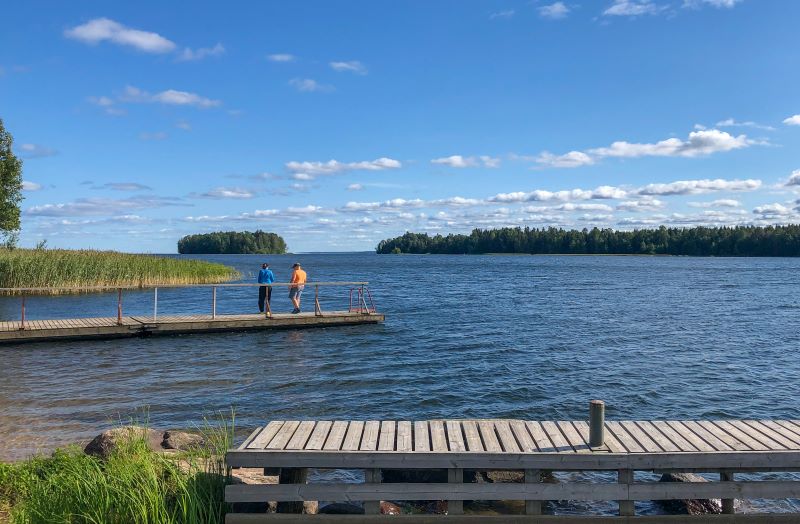Kaksi ihmistä järvimaisemissa laiturilla.
