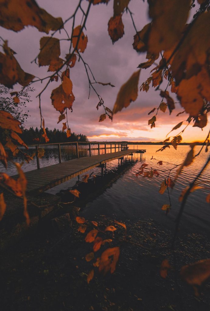 Auringonlasku Littoistenjärvellä, syksynlehtiä ja pitkälle horisonttiin kurkottava laituri.