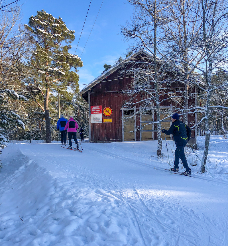 Kolme hiihtäjää ladulla ja punainen rakennus Haijaisissa.