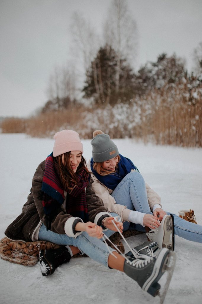 Kaksi naista pukee luistimia jalkaan järven jäällä.