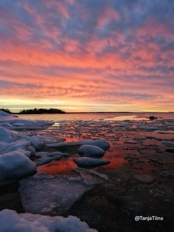 Auringonlasku värjää taivaan ja jäisen meren Raumalla.