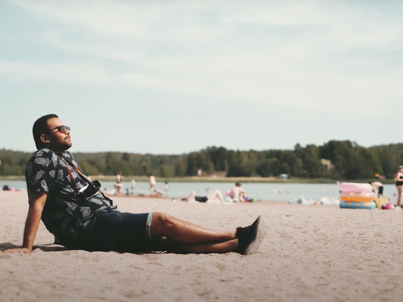 Manu istuu hiekalla Ekvallan uimarannalla ihmisten uidessa taustalla