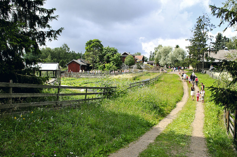 Polku täynnä ihmisiä ja Kuralan kylämäen puisia rakennuksia ja aita.