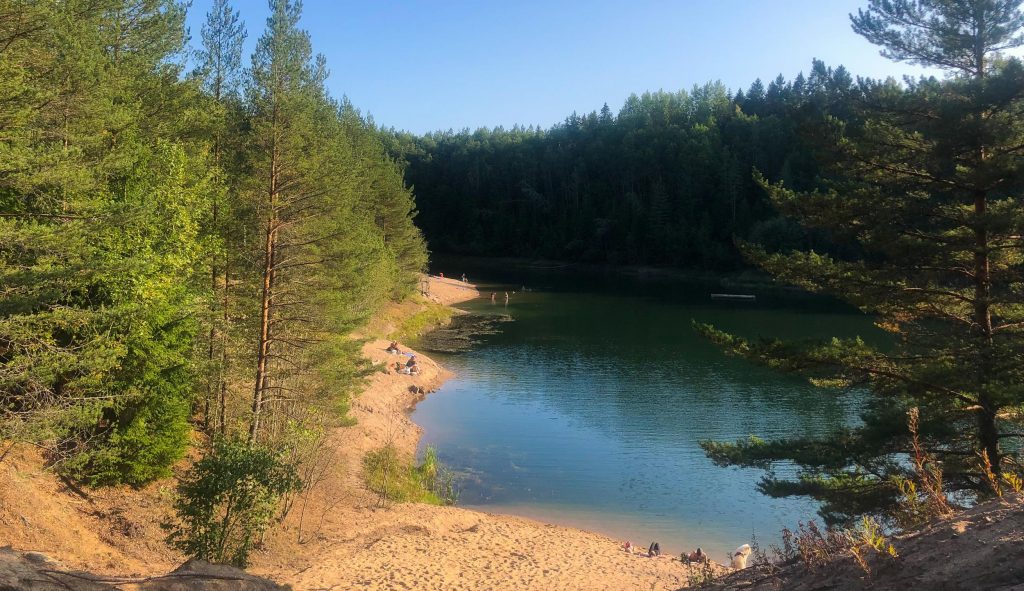Turun Jäkärlässä hiekkainen Maarian uimaranta hohtaa auringossa metsän keskellä, muutamia ihmisiä istuskelee hiekalla ja Maarianaltaan vesi on kirkasta.