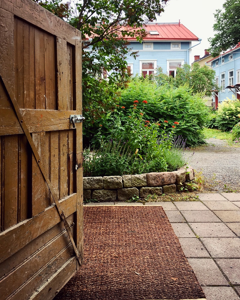 Puinen ovi, joka vie puutarhaan. Taustalla sinisiä taloja.