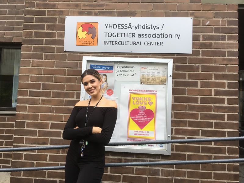 Yhdessä-yhdistyksen työntekijö seisoo tilliseinänä ja yhdistyksen kyltin edessä.