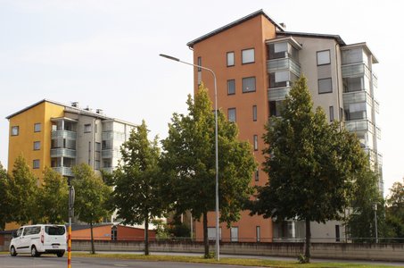 Kaksi modernia ja värikästä kerrostaloa Kerttulassa Raisiossa. Autotie ja puita etualalla.