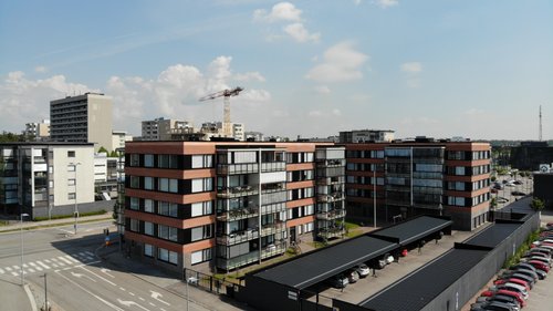 Etualalla kerrostaloja ja parkkipaikka Raision keskustassa. Rakennustyömaa taustalla.