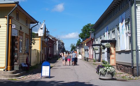 Värikkäitä puutaloja molemmin puolin lujaa Naantalin vanhassa kaupungissa. Perhe kävelee taustalla.