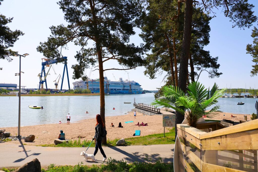 Raision Hahdenniemen uimaranta, jossa ihmisiä sekä taustalla rakenteilla oleva valtamerilaiva.