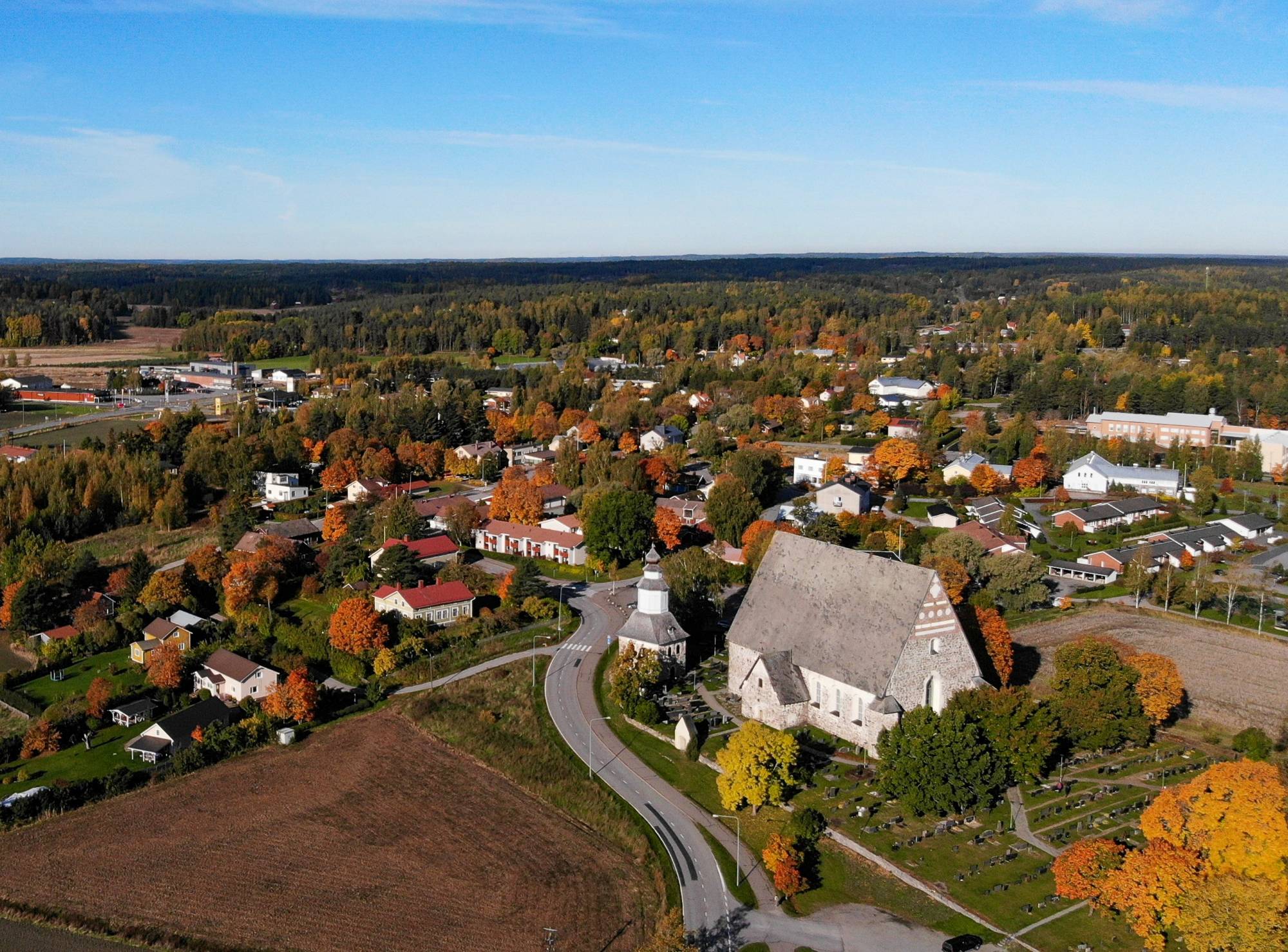 Ilmakuva Sauvon keskustasta, etualalla kivikirkko ja peltoja, taustalla pientaloasutusta.