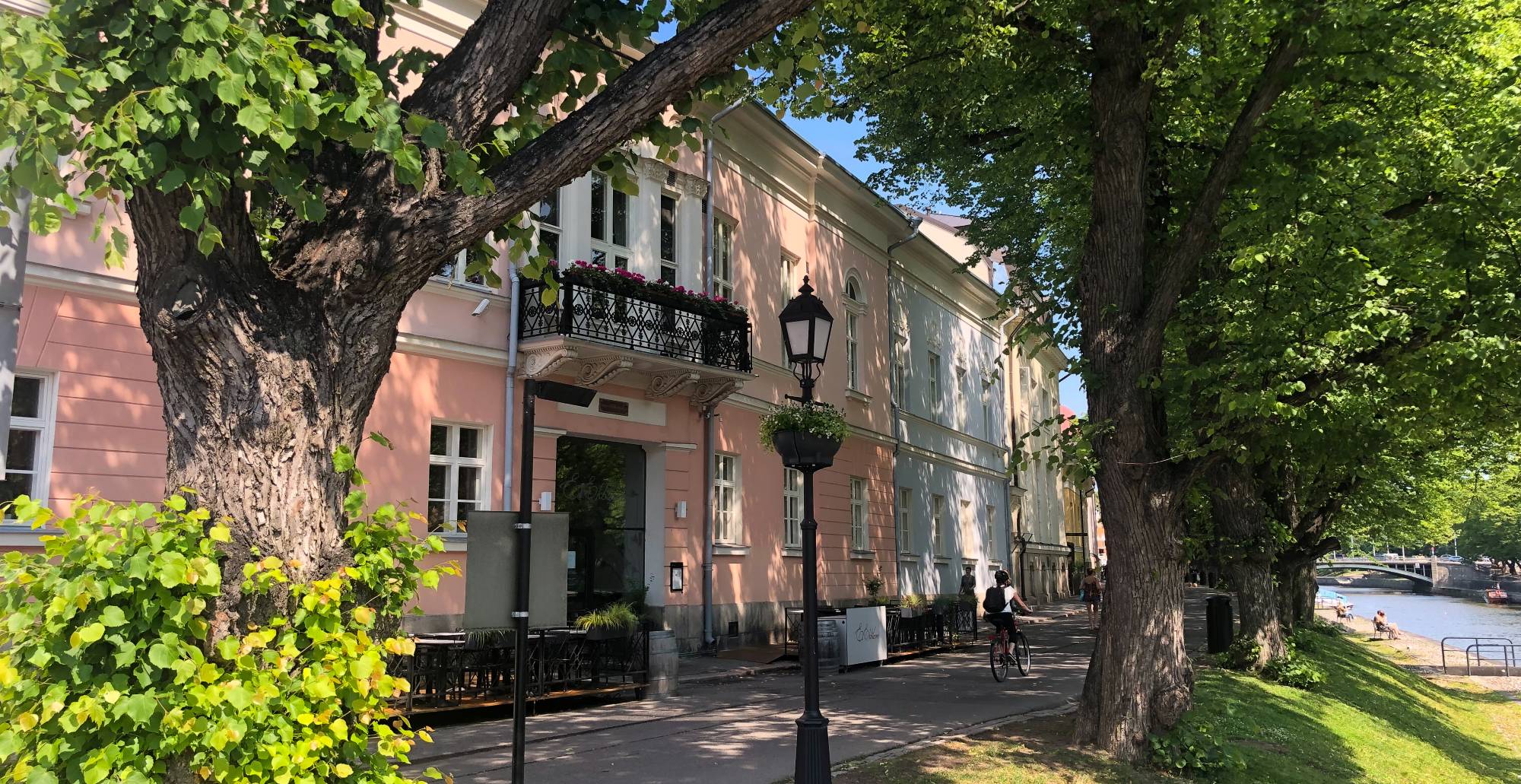 Vaaleanpunainen kivitalo ja rehevät puut Turun jokirannassa.