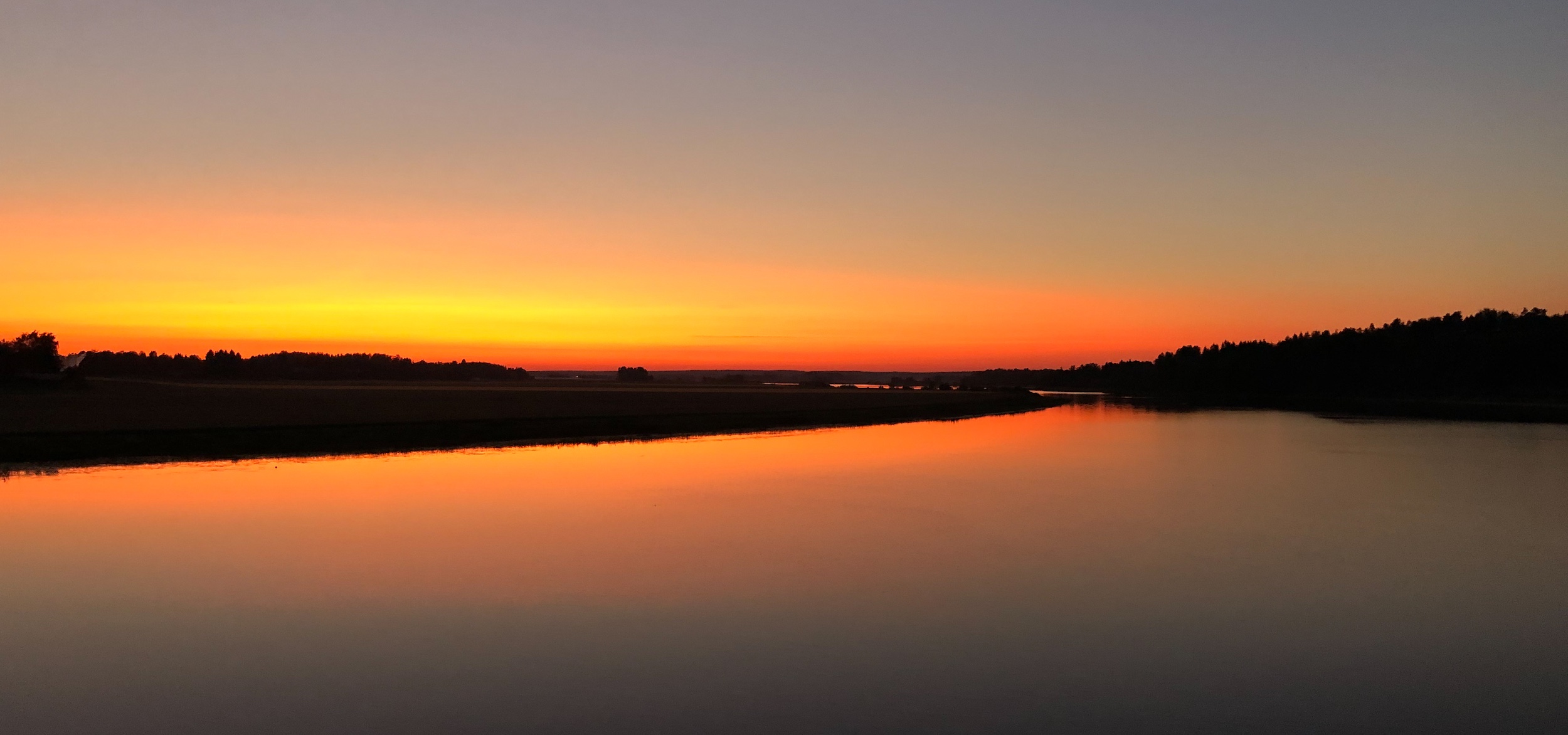 Joki kuvattuna auringonlaskussa, joka on värjännyt voimakkaasti taivaanrannan ja joen oranssiksi.